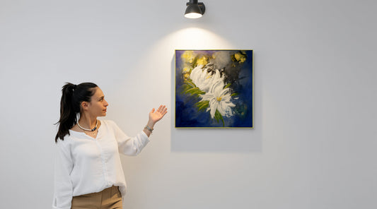 Mixed media painting "Magnify Together" by Little Haven Art Studio, in sapphire blue, white, and metallic gold, hanging on wall next to a woman viewing it under a spotlight.