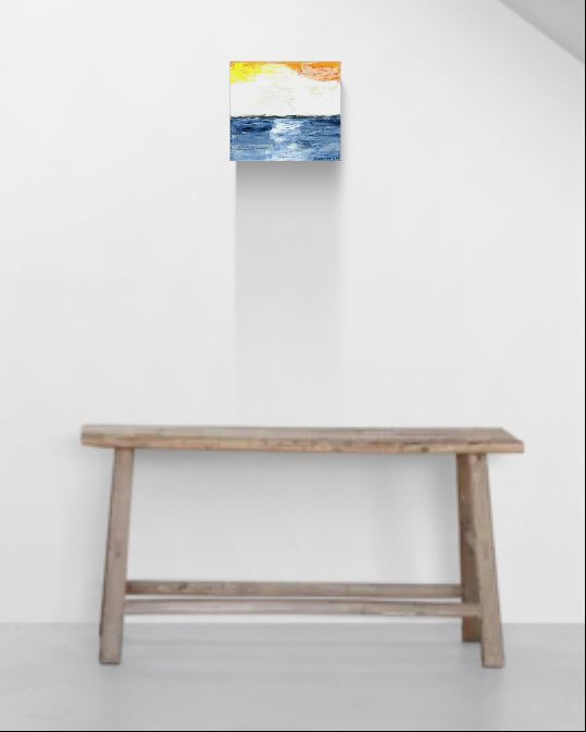 "Glow" is original abstract canvas wall art of a sunset sky over the ocean in orange, yellow, and blue, by Little Haven Art Studio, hanging above a minimalist wooden bench seat.