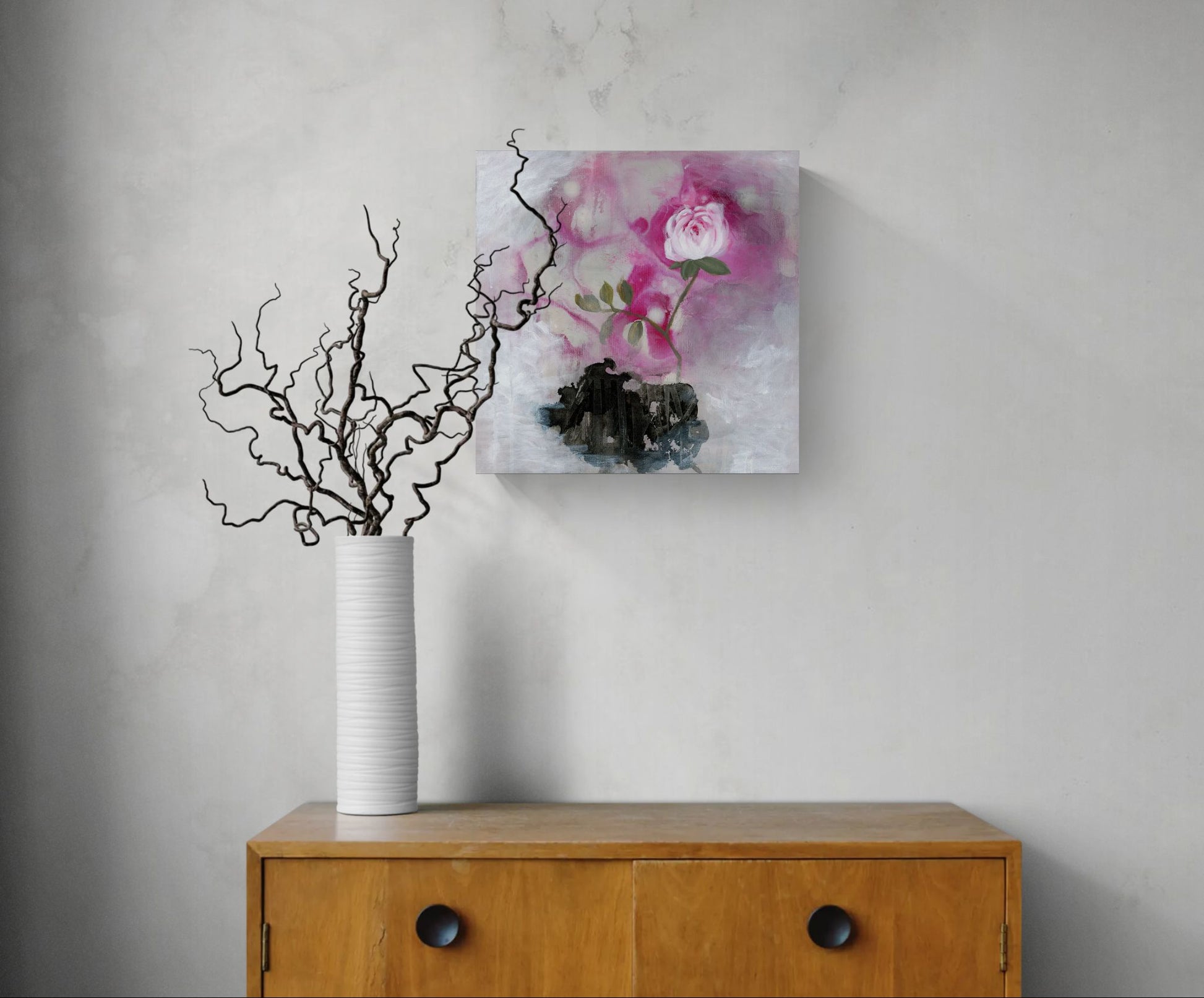 "Sanctuary Bloom" painting of a pink rose with green leaves on a textured white and black background by Amanda Craig in a hallway with desk and white vase.